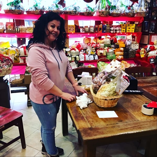 Woman smiling in Tino's Delicatessen, surrounded by Italian deli products and gift baskets.