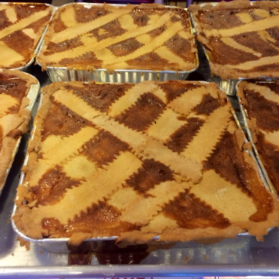 Several Italian deli pastries with lattice tops and a sweet, dark filling in foil pans.