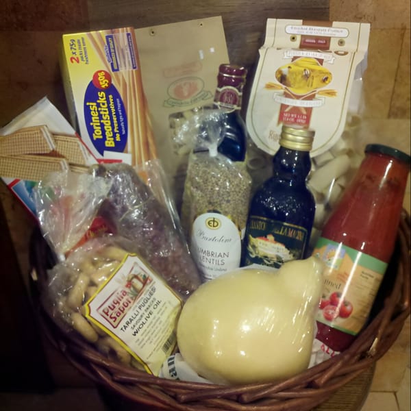 A Tino's Delicatessen gift basket filled with Italian breadsticks, pasta, lentils, olive oil, and cheese.