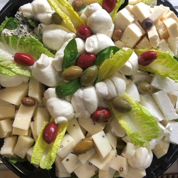 A platter of fresh mozzarella balls, cubed cheeses, olives, and lettuce at Tino's Delicatessen.