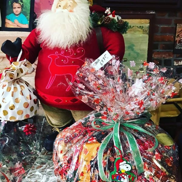 A Santa Claus doll stands next to two large, festive gift baskets wrapped in clear plastic.