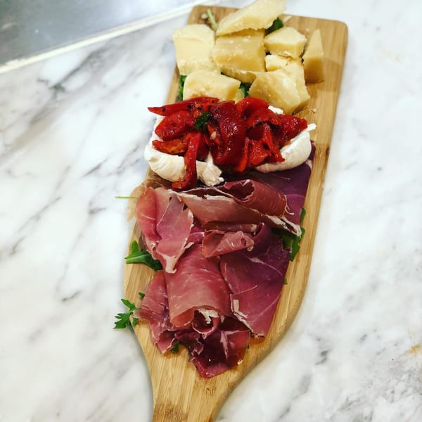 Tino's Delicatessen charcuterie board with prosciutto, burrata, roasted red peppers, and Parmesan cheese.