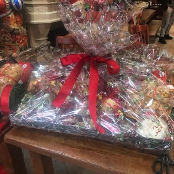 A large gift basket filled with Italian deli items, wrapped in clear cellophane with a red bow.
