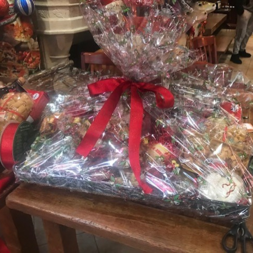 A large gift basket filled with Italian deli items, wrapped in clear cellophane with a red bow.